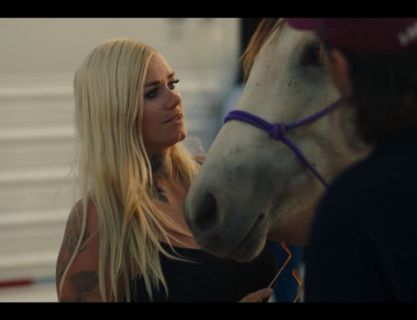 Elderly woman with tattoos touching a white horse's face, sharing a heartfelt moment.